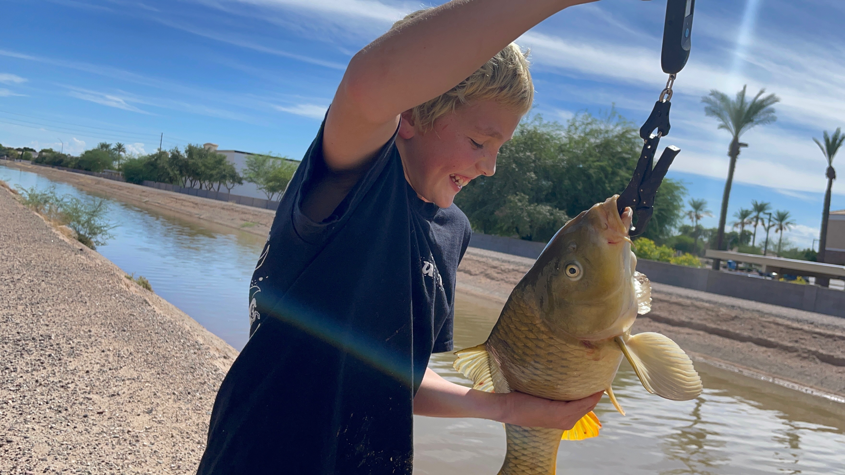 Lucas holding an 8-pound carp on a scale grip by a canal in Mesa